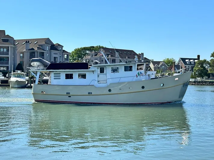 La Vita Marina Yacht Photos Pics Custom Holland Marine 50 Trawler, 1993, cruising in a calm harbor with buildings in the background.