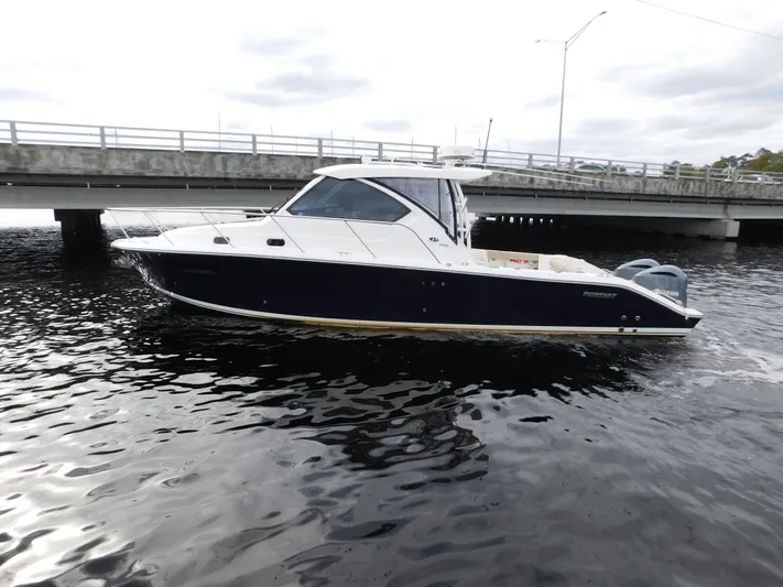  Yacht Photos Pics 2018 Pursuit OS 325 Offshore boat cruising near a bridge on a cloudy day.