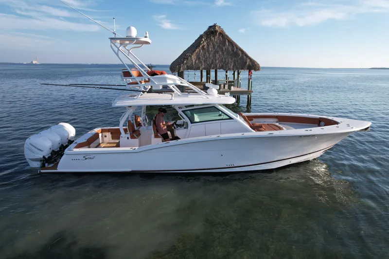  Yacht Photos Pics 2019 Scout 420 LXF boat on calm water near a thatched-roof dock.