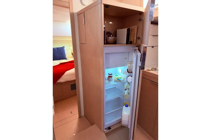 One Five Yacht Photos Pics Open fridge in 2022 Beneteau Oceanis Yacht 54, showcasing interior storage and adjacent cabin.