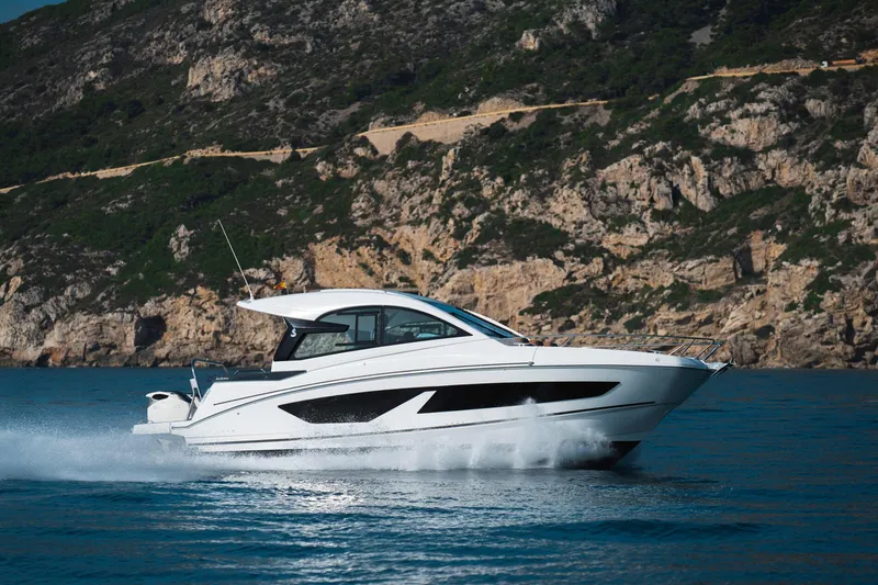  Yacht Photos Pics 2025 Beneteau Gran Turismo 32 Outboard cruising on blue water near rocky coastline.