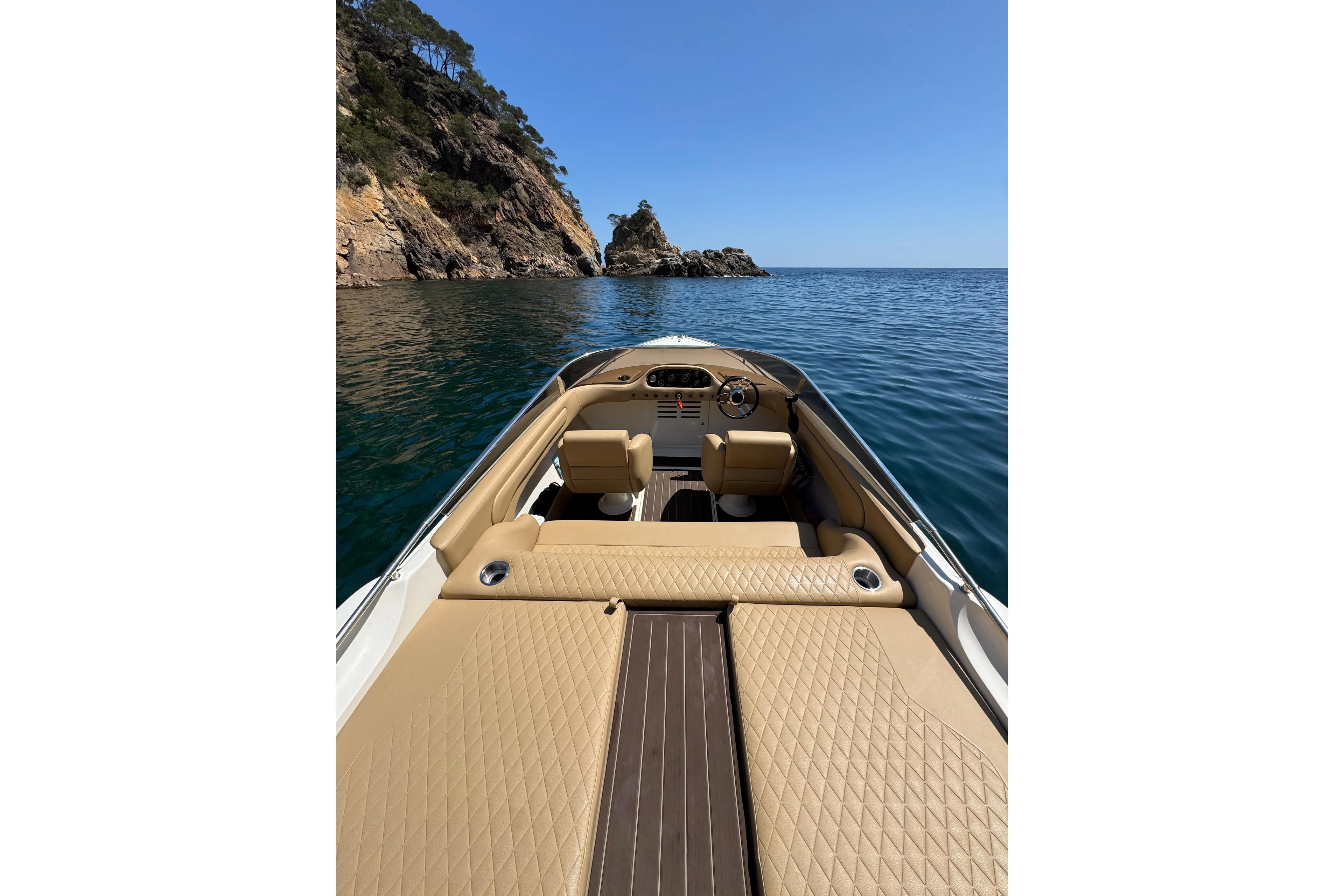 Luxury Performance 607 boat interior with tan seating, cruising near rocky coastline, clear blue sea.