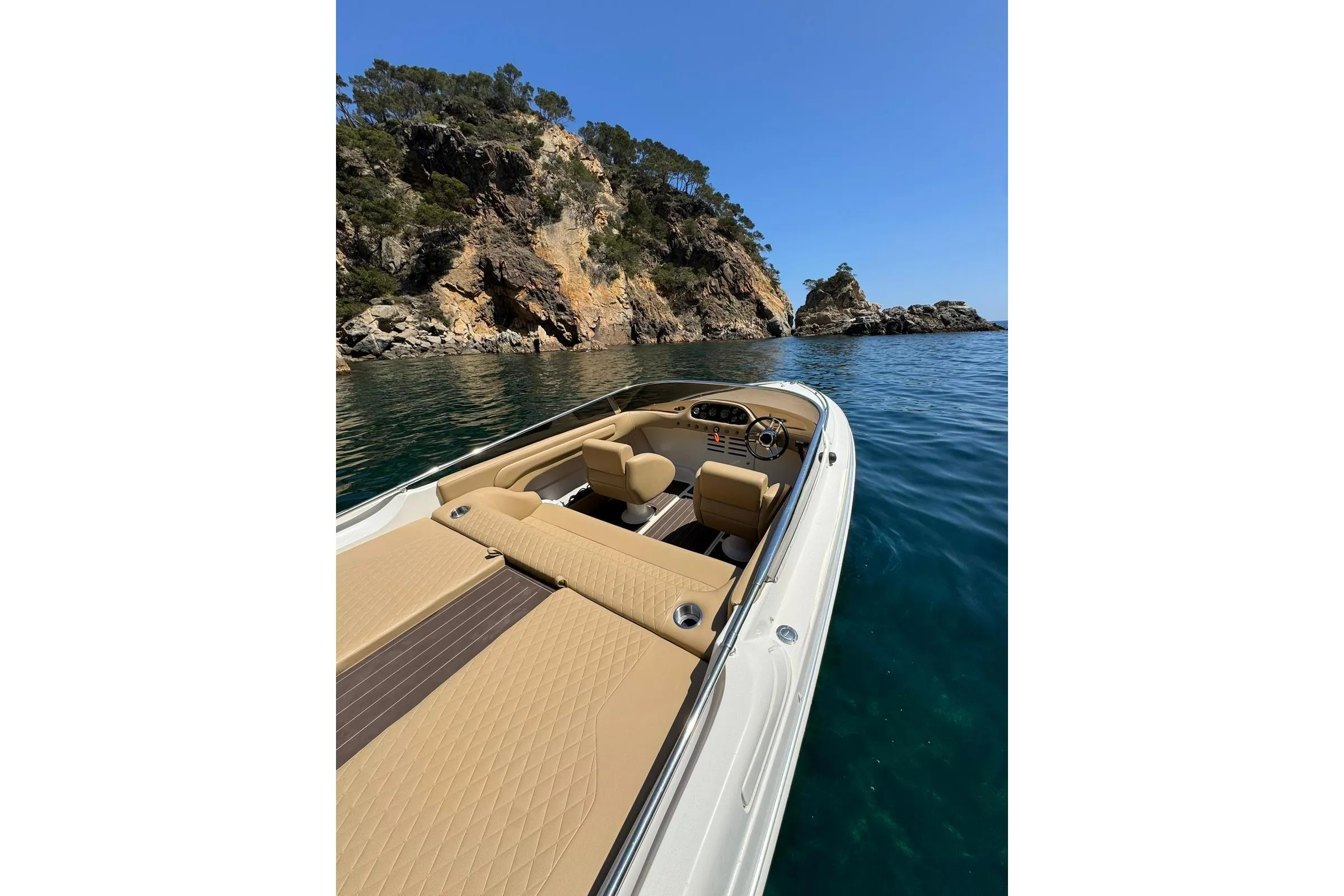 Luxury Performance 607 boat cruising near rocky coastline, clear blue sky, and calm waters.