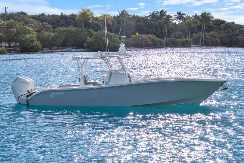  Yacht Photos Pics 2026 Yellowfin 32 Offshore boat on sparkling blue water, surrounded by lush greenery.