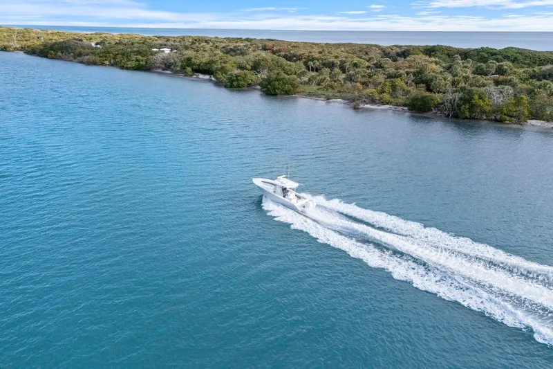  Yacht Photos Pics 2026 Yellowfin 32 Offshore boat cruising on blue water near a lush shoreline.