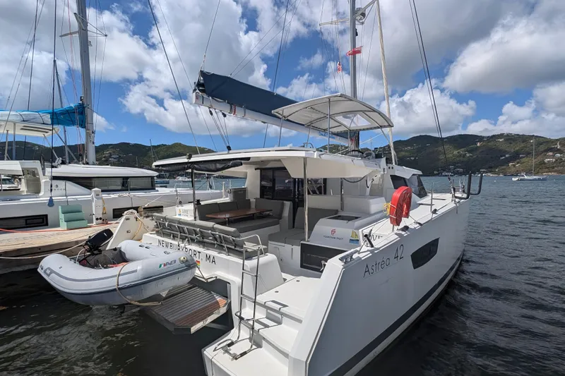 Love A Fayre Yacht Photos Pics 2020 Fountaine Pajot Astrea 42 catamaran docked with inflatable dinghy, scenic coastal backdrop.