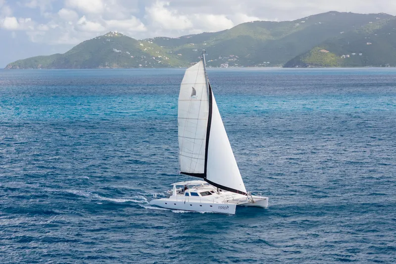 Osprey Yacht Photos Pics Sailing catamaran Voyage 520, 2010 model, cruising in clear blue ocean near lush green islands.