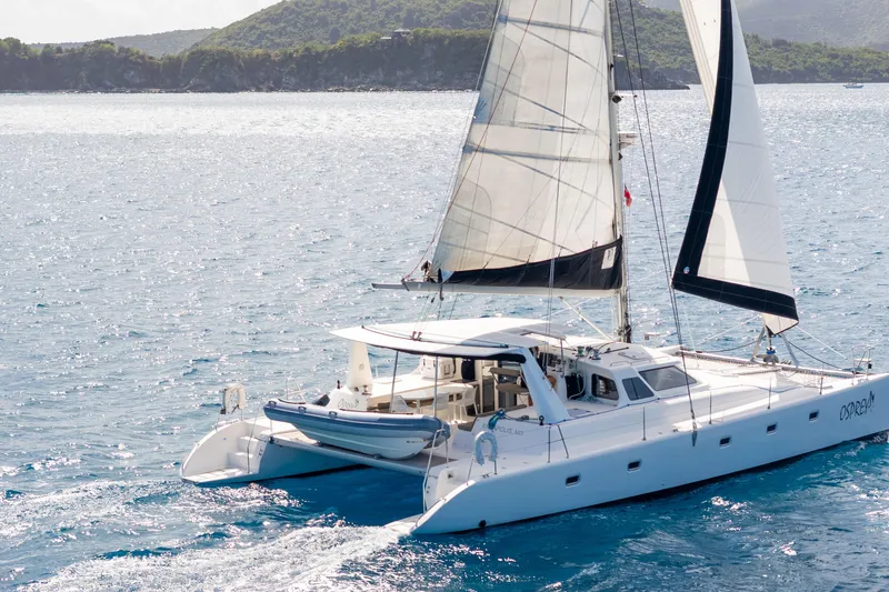 Osprey Yacht Photos Pics Sailing catamaran Voyage 520, 2010 model, cruising on clear blue waters near a lush coastline.