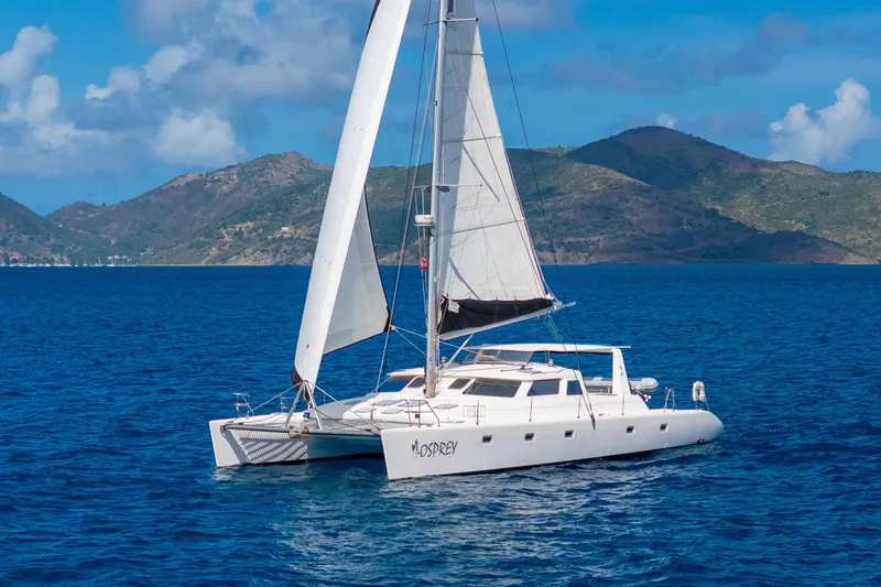 Osprey Yacht Photos Pics Sailing catamaran Voyage 520, 2010 model, cruising in clear blue waters with scenic mountain backdrop.