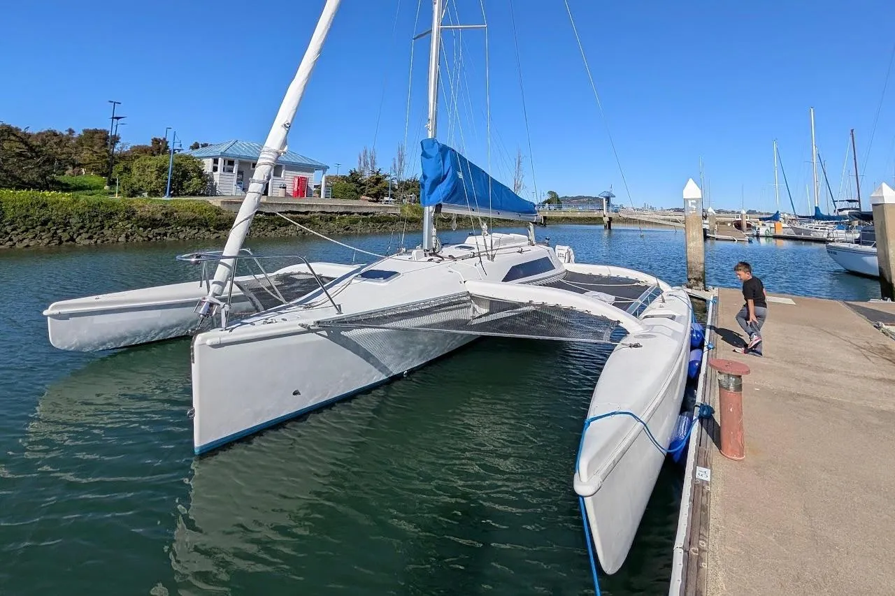 1996 Corsair F-31 trimaran docked in a marina with blue sail and clear sky.