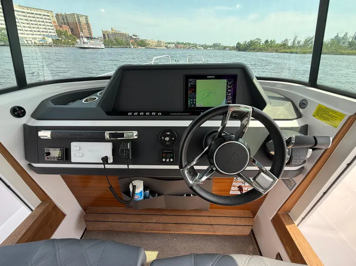  Yacht Photos Pics 2021 Axopar 28 CABIN helm with steering wheel and navigation display on a calm waterway.