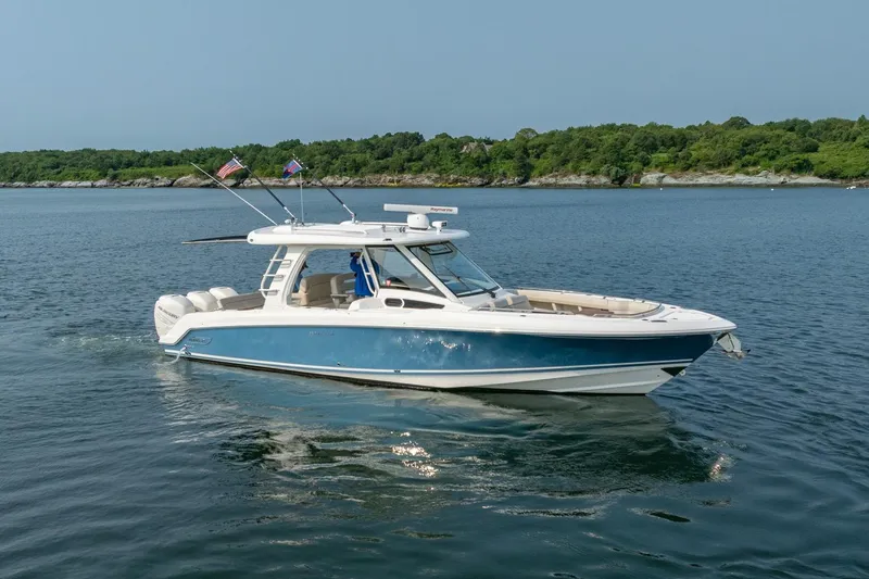 Blue Skies Yacht Photos Pics 2019 Boston Whaler 350 EX REALM boat cruising on calm water with lush green shoreline.