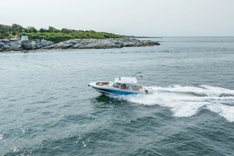 Blue Skies Yacht Photos Pics 2019 Boston Whaler 350 EX REALM cruising near rocky shoreline and lighthouse.