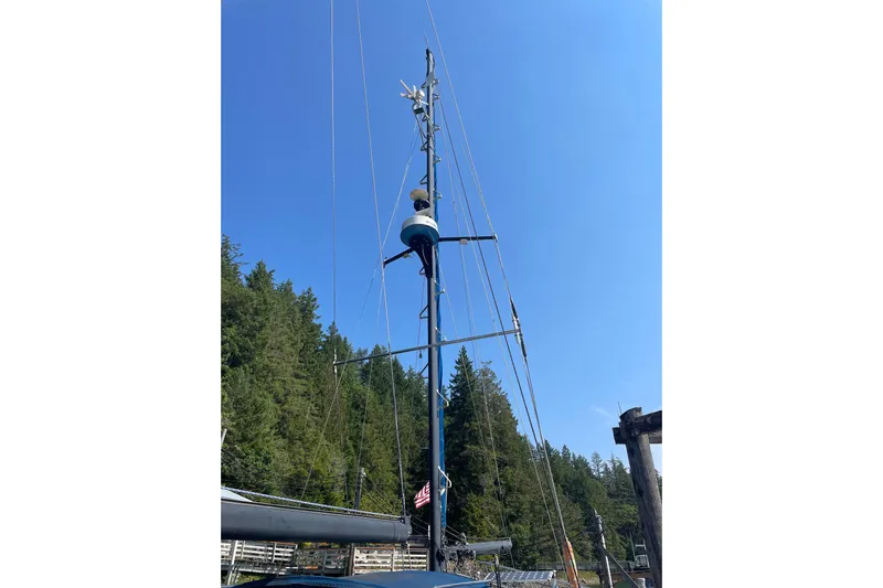 Sun Dazzler Yacht Photos Pics 1981 Mariner 48 sailboat mast against clear blue sky and forest backdrop.