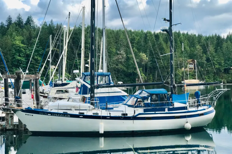 Sun Dazzler Yacht Photos Pics 1981 Mariner 48 sailboat docked in a serene marina with forest backdrop.