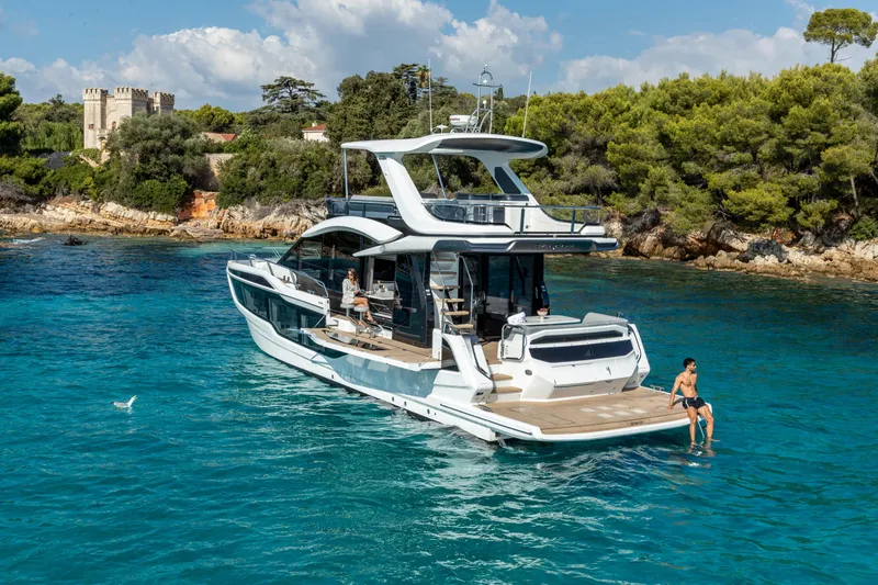  Yacht Photos Pics 2026 Galeon 560 Fly yacht cruising near a scenic coastline with lush greenery.