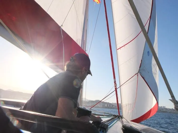  Yacht Photos Pics Person sailing NEEL 51 trimaran, 2017 model, with sunlit sails and coastal backdrop.