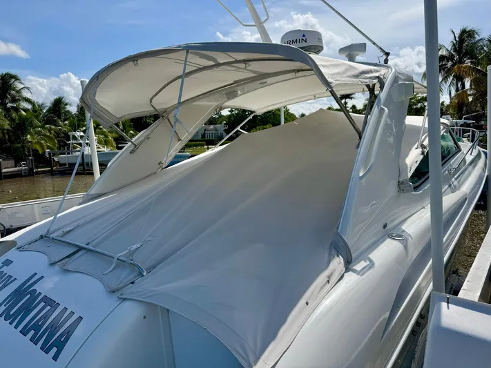Tony Montana Yacht Photos Pics 1999 Formula 400 Super Sport boat docked, covered with a white canopy, surrounded by palm trees.