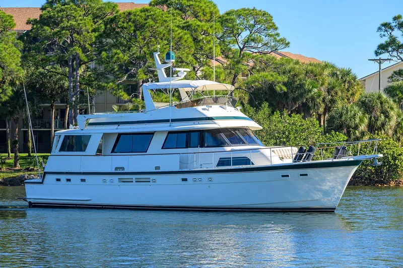 Phantom Yacht Photos Pics 1987 Hatteras 63 Motor Yacht cruising on a serene waterway, surrounded by lush greenery.