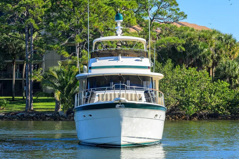 Phantom Yacht Photos Pics 1987 Hatteras 63 Motor Yacht on calm water, surrounded by lush greenery.