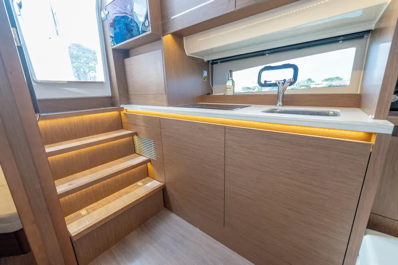  Yacht Photos Pics Modern kitchen area in 2022 Jeanneau Leader 12.5 WA yacht with wooden cabinetry and stairs.