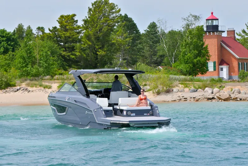  Yacht Photos Pics 2026 Cruisers Yachts 34 GLS I/O cruising near a scenic lighthouse and lush greenery.