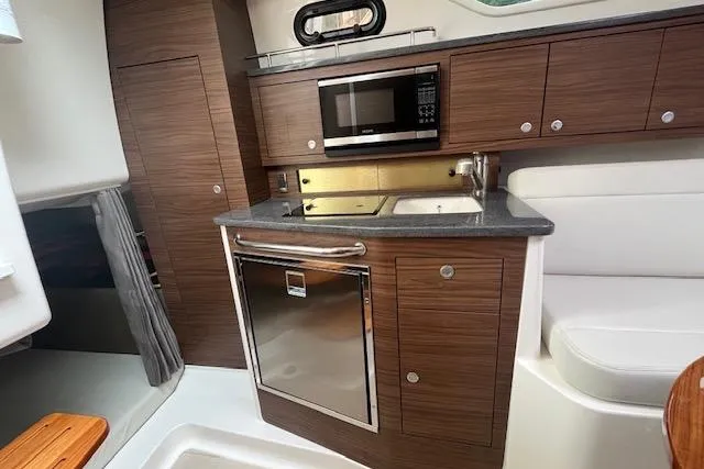  Yacht Photos Pics 2020 Boston Whaler 325 Conquest interior kitchen with microwave, sink, and wooden cabinetry.