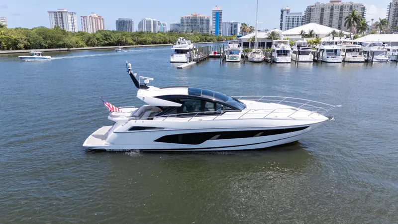 Brew Crew Yacht Photos Pics 2022 Sunseeker Predator 60 yacht cruising in a marina with city skyline backdrop.