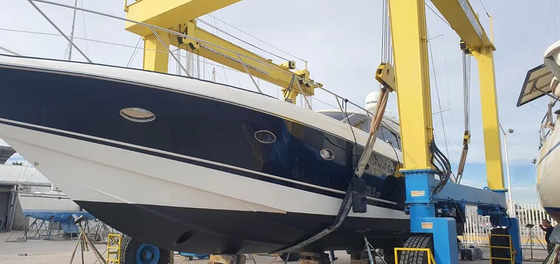 Burn N Daylight Yacht Photos Pics Sunseeker Predator 58 yacht from 1999 in dry dock, supported by a yellow gantry crane.