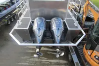 Twin outboard motors on a 2023 Robust LC1227 boat, docked near construction equipment.