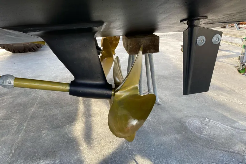  Yacht Photos Pics Close-up of a 2003 Mochi 2250 boat propeller and rudder on a concrete surface.