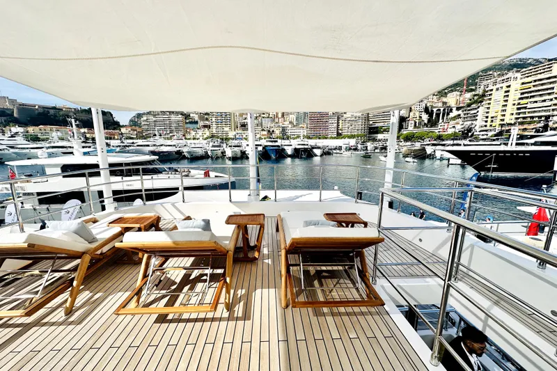 Optimism Yacht Photos Pics Luxurious 2023 Majesty 120 yacht deck with sun loungers, overlooking a marina.