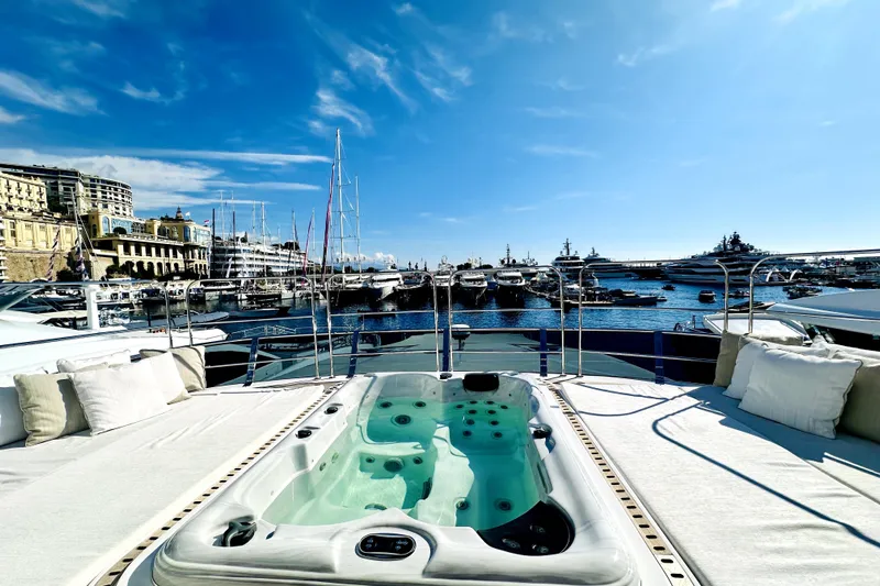 Optimism Yacht Photos Pics Luxurious 2023 Majesty 120 yacht with jacuzzi, docked in a scenic marina under a clear blue sky.