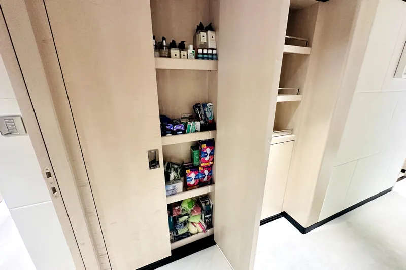 Optimism Yacht Photos Pics Modern pantry shelves in a 2023 Majesty 120 yacht, stocked with toiletries and snacks.