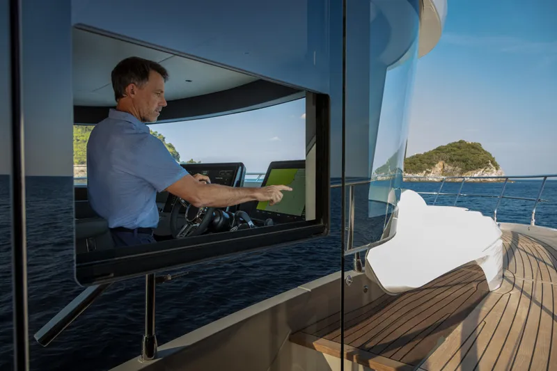 Absolute Navetta 64 Yacht Photos Pics Man operating Absolute Navetta 64 yacht, 2025 model, on open sea with island view.