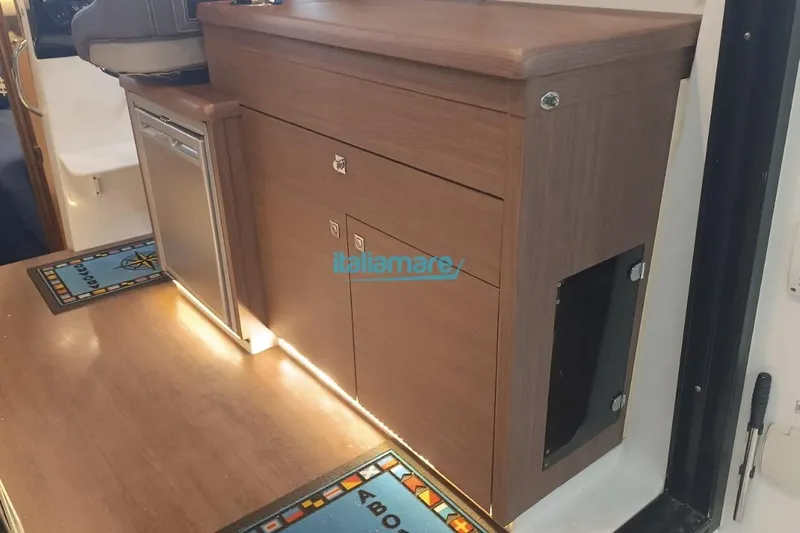  Yacht Photos Pics 2019 Jeanneau Merry Fisher 895 interior with wooden cabinetry and compact fridge.