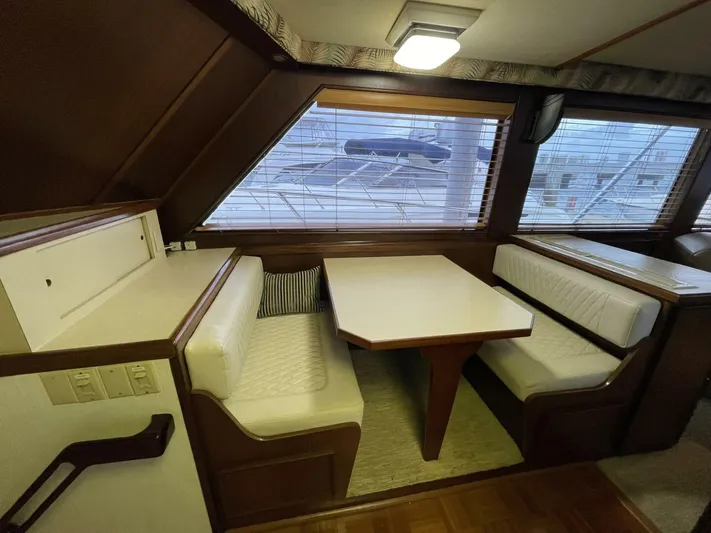 Moonshine Yacht Photos Pics 1985 Hatteras Enclosed Bridge interior with dining area, featuring white cushioned seating and wooden table.
