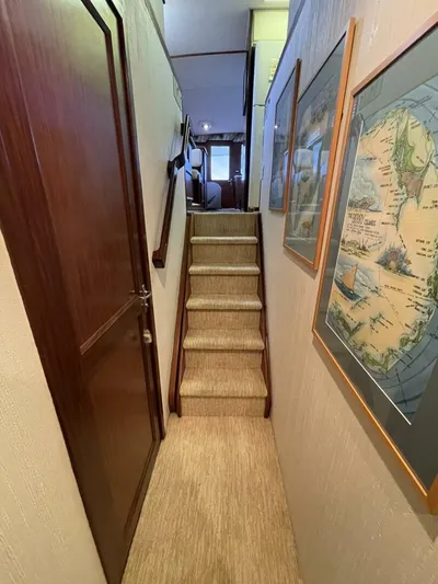 Moonshine Yacht Photos Pics Narrow hallway with stairs in a 1985 Hatteras Enclosed Bridge yacht, featuring framed maps.