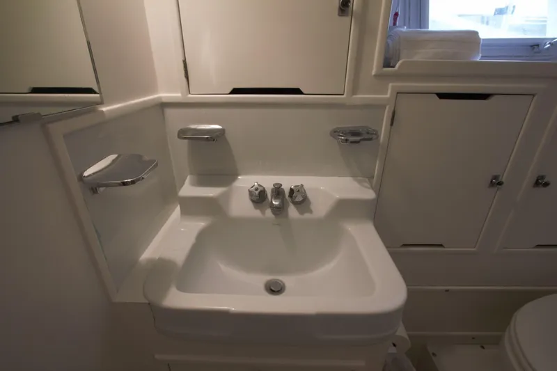  Yacht Photos Pics Compact white bathroom sink in 1963 Huckins Linwood yacht, featuring chrome fixtures and storage cabinets.