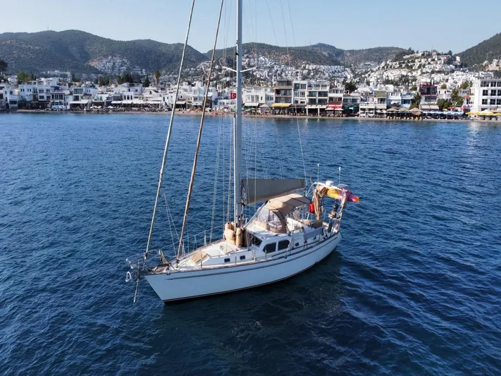 Tutkum Yacht Photos Pics Sailboat Tayana 48 (2007) anchored in scenic coastal waters with hillside town backdrop.