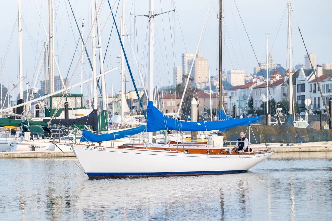 Vintage 1938 Philip Rhodes Cutter sailboat docked in a marina with cityscape background.