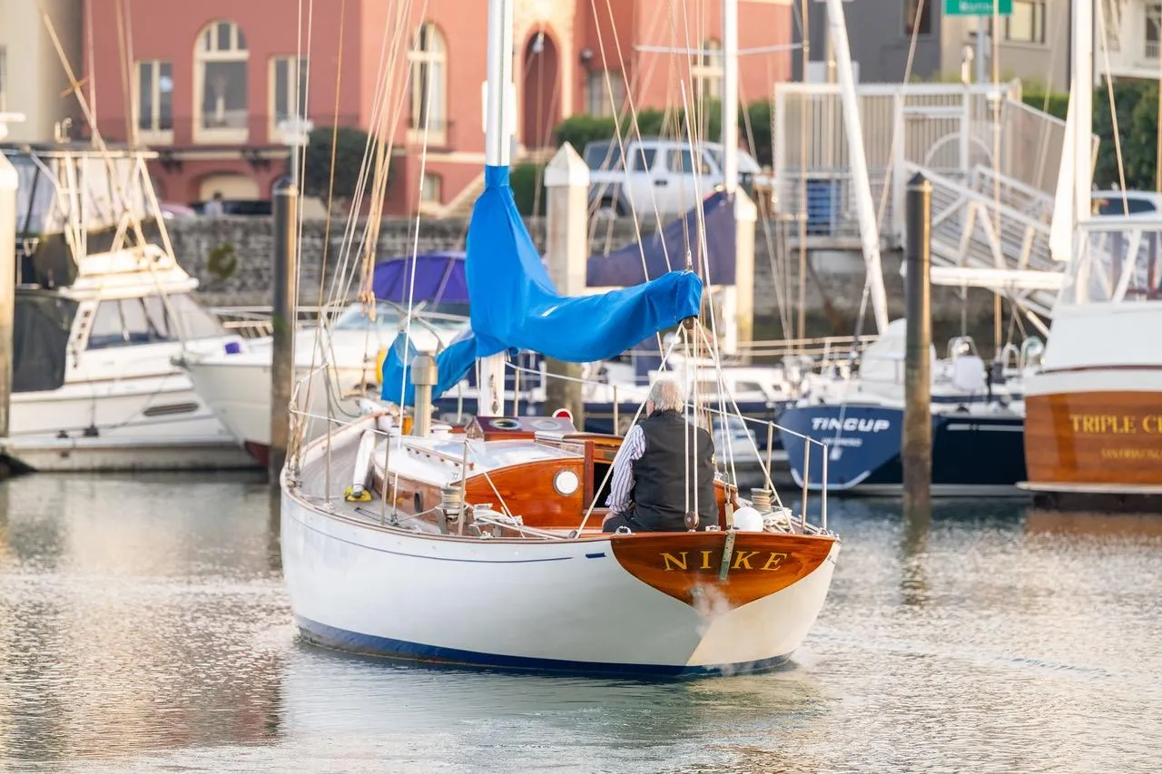Vintage 1938 Philip Rhodes Cutter sailboat in marina, featuring wooden design and blue sail.