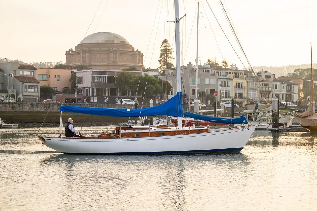 Vintage 1938 Philip Rhodes Cutter sailboat on calm water near urban waterfront.