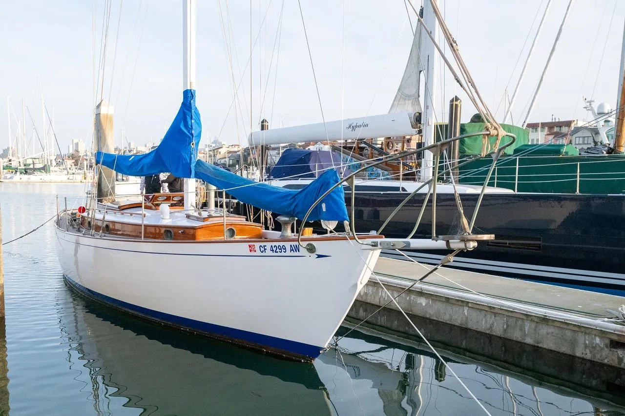 Vintage 1938 Philip Rhodes Cutter sailboat docked in a marina, featuring blue sail covers.