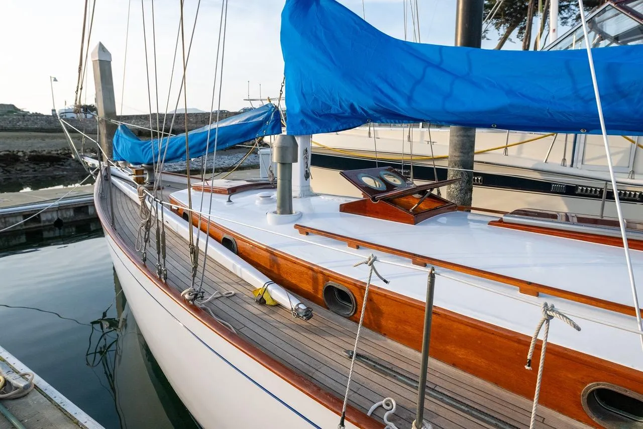 Vintage 1938 Philip Rhodes Cutter sailboat with blue sail cover docked at marina.