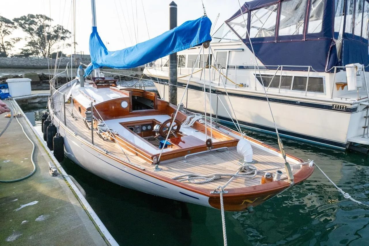 1938 Philip Rhodes Cutter sailboat docked, featuring classic wooden design and blue sail cover.