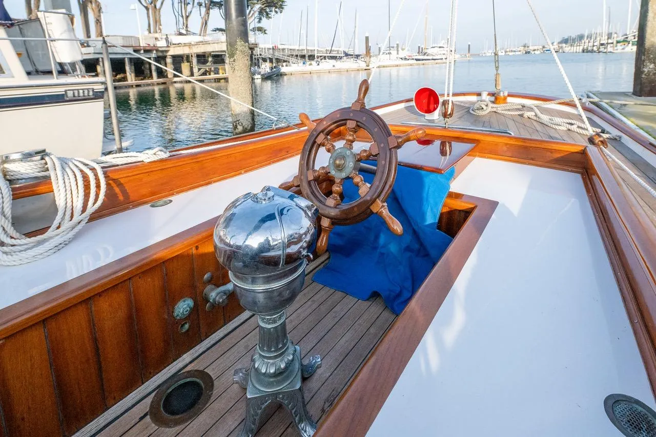 1938 Philip Rhodes Cutter sailboat with wooden deck and classic steering wheel.
