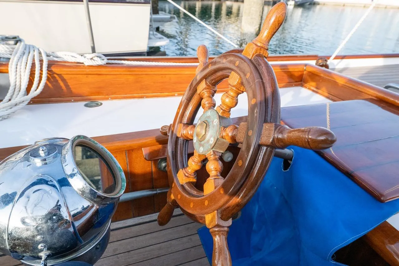 Wooden steering wheel of a 1938 Philip Rhodes Cutter sailboat, with polished metal compass nearby.