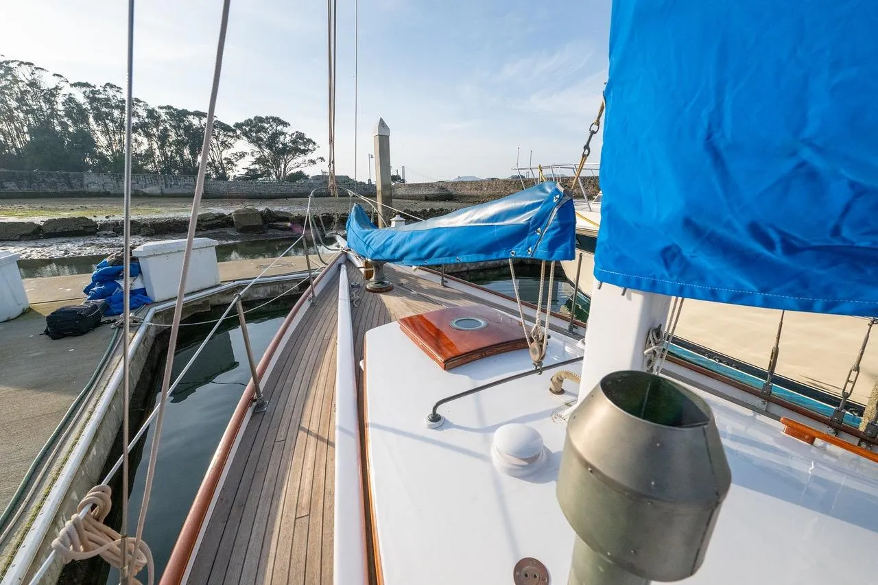 Vintage 1938 Philip Rhodes Cutter sailboat docked, featuring wooden deck and blue sail cover.