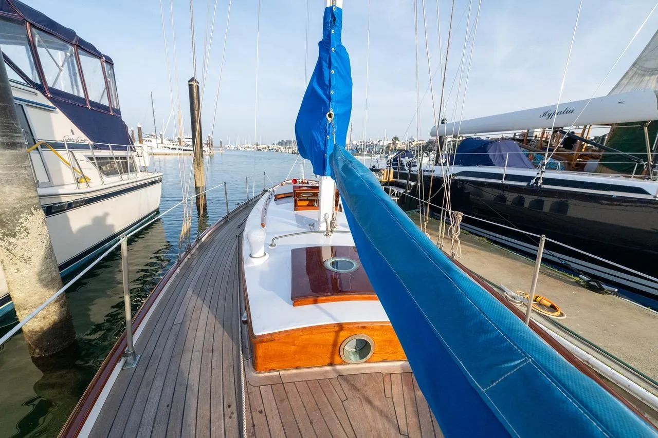 Classic 1938 Philip Rhodes Cutter sailboat docked at marina, featuring wooden deck and blue sail cover.
